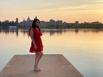 Woman standing on lake against sky during sunset