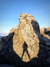 Shadow of person on rock against blue sky