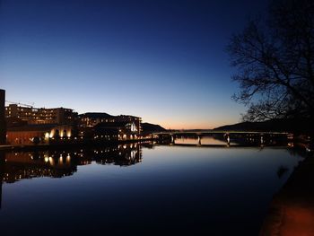 Illuminated buildings by river against sky at dusk