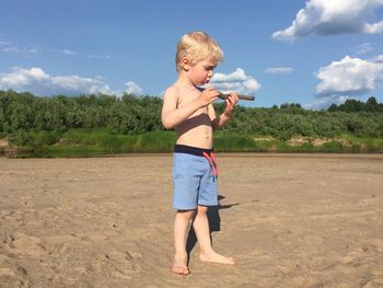 Full length of shirtless boy standing against sky