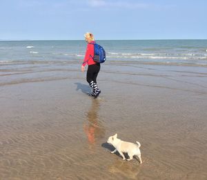 Full length of woman with dog walking on shore at beach against sky