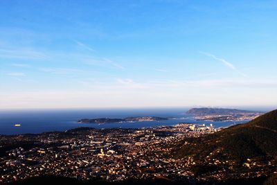 Aerial view of city by sea against blue sky