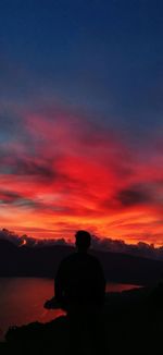 Rear view of silhouette man sitting against orange sky