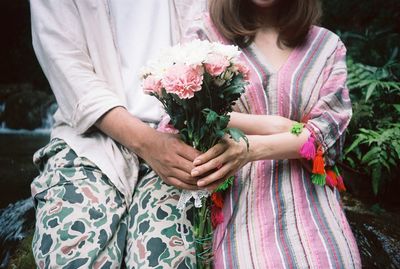 Midsection of couple holding flower bouquet while sitting outdoors