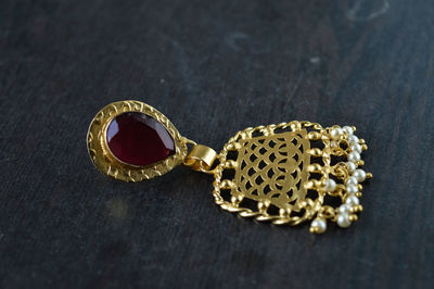 A indian jewelry ear piece with red stone isolated on black and grey texture wooden table