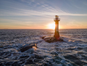 Lighthouse by sea against sky during sunset