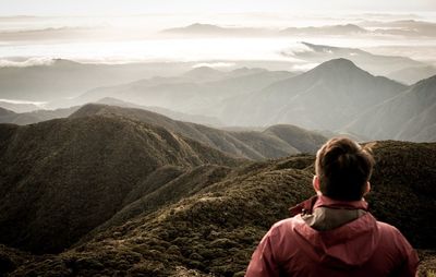 Rear view of man looking at mountains against sky