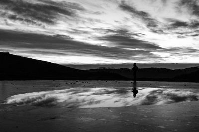 Silhouette man standing on beach against sky during sunset