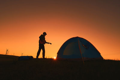 Man playing guitar by tent against sky during sunset