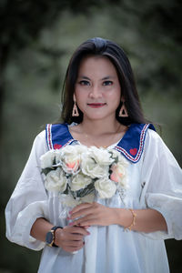 Portrait of smiling young woman standing against trees