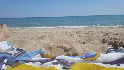 Low section of person on beach against clear blue sky