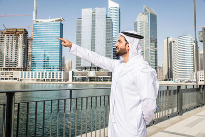 Side view of businessman standing by river against buildings