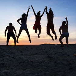 Rear view full length of friends jumping on landscape against sky during sunset