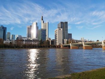 Modern buildings by river against sky in city