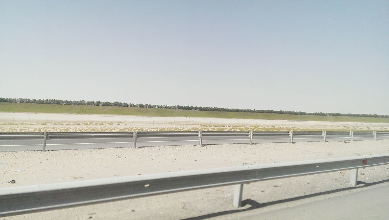 clear sky, copy space, tranquil scene, tranquility, water, road, nature, scenics, landscape, beauty in nature, day, railing, outdoors, field, no people, grass, sea, sky, transportation, beach