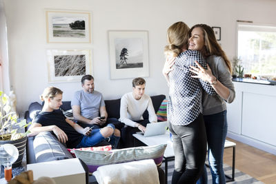 Mother and daughter embracing while family sitting on sofa in living room