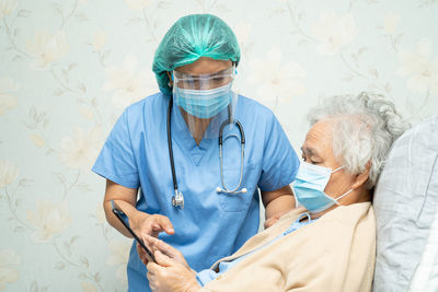 Senior woman wearing flu mask holding digital tablet with doctor at hospital