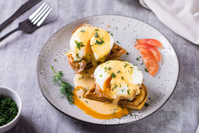 Delicious homemade breakfast with waffles, bacon and eggs benedict on a plate.