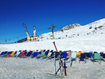 Deck chairs on snow covered mountain against blue sky