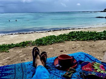 Low section of woman relaxing on beach against sky