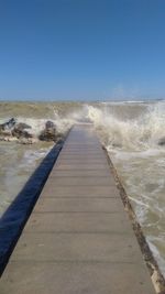 Footpath leading towards sea against clear blue sky