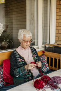 High angle view of elderly woman knitting while sitting on bench at porch