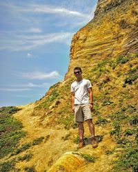 Low angle portrait of young man wearing sunglasses standing on mountain during sunny day