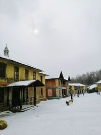 Houses on snow covered field by buildings against sky