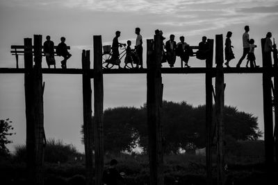 Silhouette people on wooden footbridge against sky during dusk