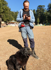 Full length of a european man using phone in outdoor with sitting dog