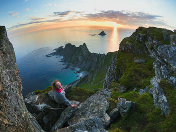 Woman sitting on rock against sky during sunset