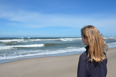 Rear view of girl standing at beach against blue sky