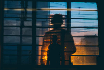 Rear view of silhouette man reflecting on window