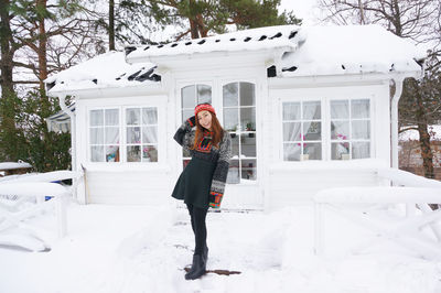 Full length portrait of young woman standing on snow covered house