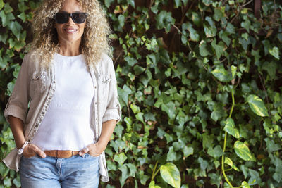 Smiling woman standing against hedge