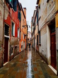 Wet street amidst houses against sky