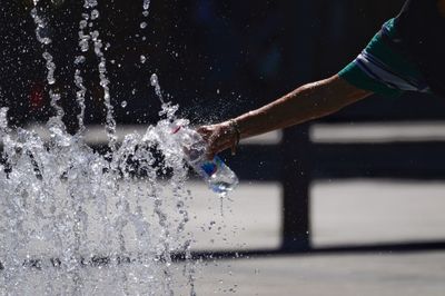 Cropped hand of man filling bottle in splashing water fountain