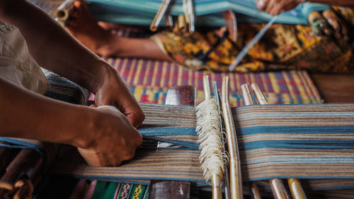 Cropped hands weaving with loom in factory
