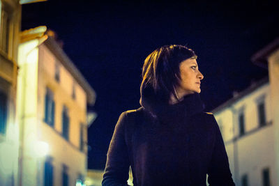 Woman looking at illuminated building in city at night