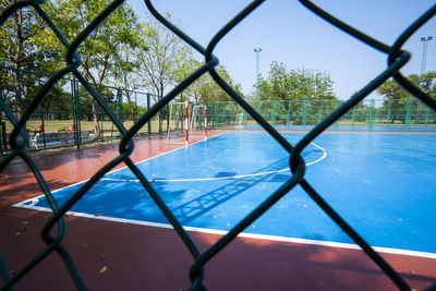 Swimming pool by trees seen through chainlink fence