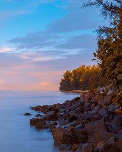 Rocks by sea against sky during sunset