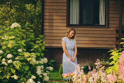 Full length of smiling woman standing against house