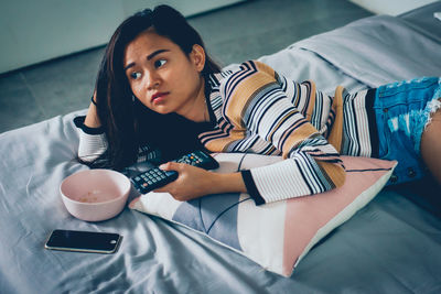 Midsection of woman sitting on sofa at home holding a tv remote. 