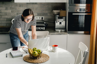 Side view of young woman sitting on table at home