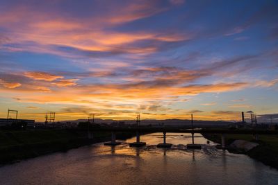 Silhouette bridge over river against sky during sunset