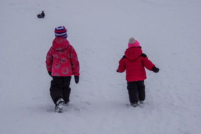 Rear view of siblings walking on snow covered field