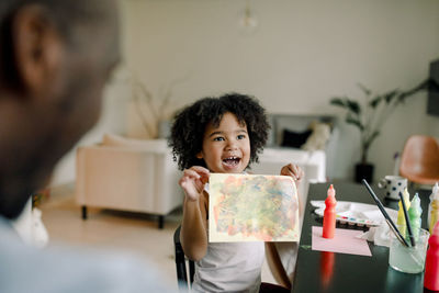 Cheerful daughter showing painting to father at home