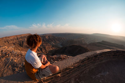 Woman sitting on mountain against sky