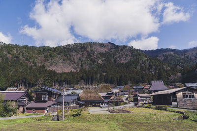 Houses on field by buildings against sky