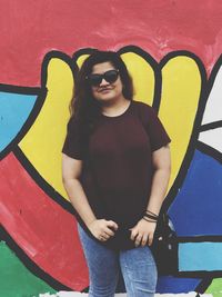 Young woman wearing sunglasses standing against wall